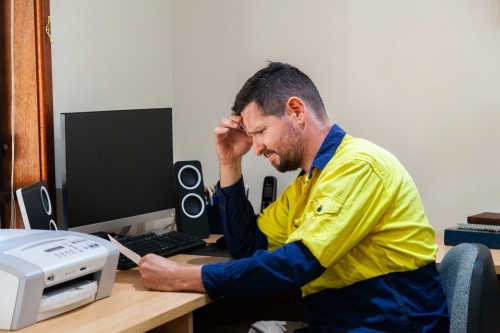 Male tradie in his 30's sitting at his computer stressed out over paperwork - Australian Stock Image