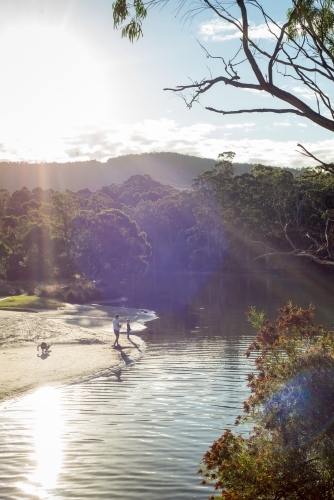 Man and boy fishing at river outlet with sun ray light - Australian Stock Image