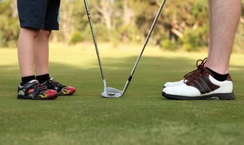 Man and child legs and shoes with golf clubs on green