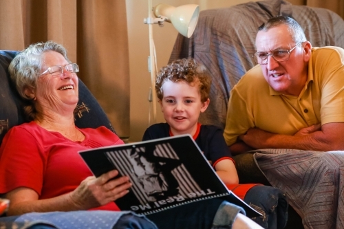 Man and woman laughing with young child on lounge in house - Australian Stock Image