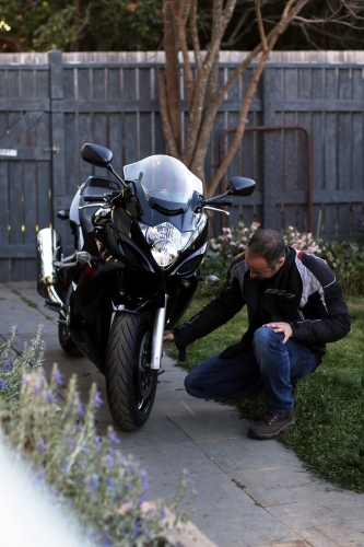 Man crouching next to motorbike in garden - Australian Stock Image