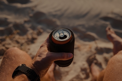 Man holding a can of drink at sunset on the beach, point of view angle (POV). - Australian Stock Image