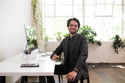 Man in a suit sitting at a desk in a creative warehouse studio - Australian Stock Image