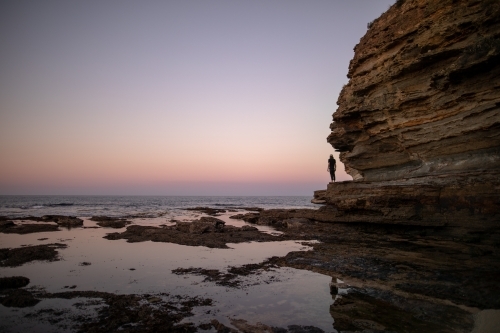 Man in Distance Standing on Rocks Overlooking The Ocean - Australian Stock Image