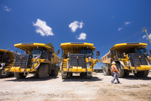 Man in high visibility clothing walking in front of haul trucks. - Australian Stock Image