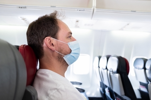 Man on an airplane wearing a surgical mask traveling during the COVID-19 coronavirus pandemic - Australian Stock Image