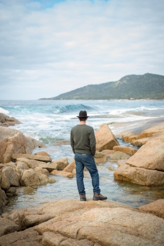 Man on boulder rocks at beach - Australian Stock Image