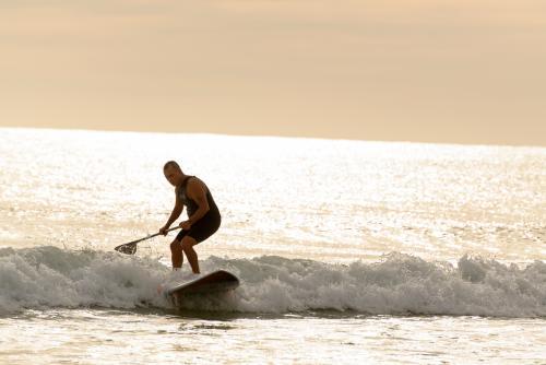 Man on paddleboard riding wave and backlit by dawn light - Australian Stock Image