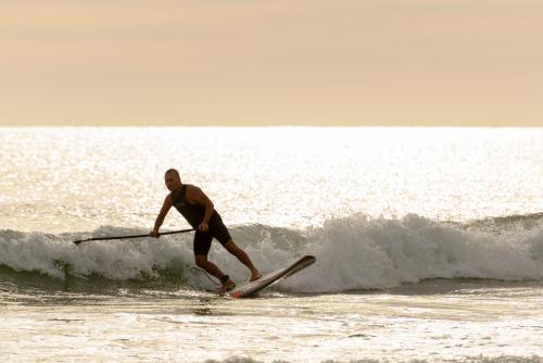 Man on paddleboard riding wave and backlit by dawn light on glistening water - Australian Stock Image