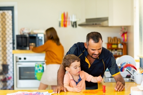 man playing with toddler in kitchen with woman in background