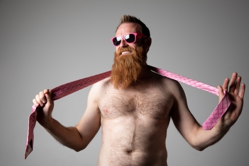Man posing for photographs, shirtless with a pink tie and sunglasses