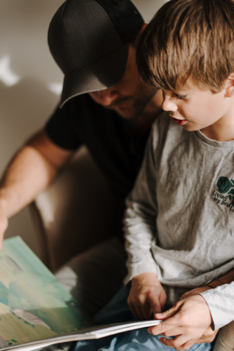 Man reading stories to his son while sitting on the couch. - Australian Stock Image