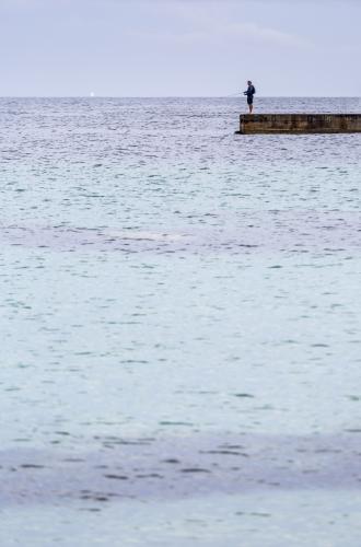 Man recreational fishing on the end of a concrete pier - Australian Stock Image