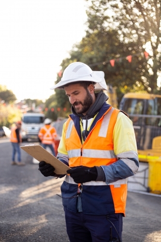 man road worker with beard and white hat wearing yellow jacket looking at his notes - Australian Stock Image