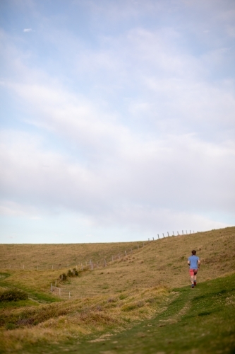 Man Running Uphill From Distance Under Blue Sky - Australian Stock Image