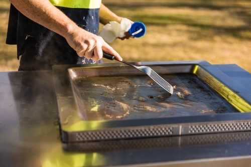 Man's hand holding scraper cleaning barbecue - Australian Stock Image