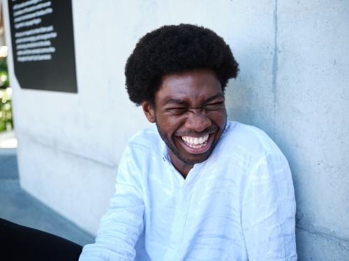 Man sitting against a concrete wall laughing