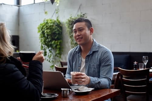 Man sitting at table at restaurant talking with friend - Australian Stock Image