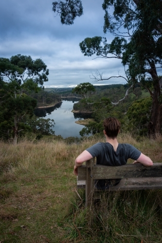 Man Sitting on Bench above a lake on a stormy afternoon - Australian Stock Image