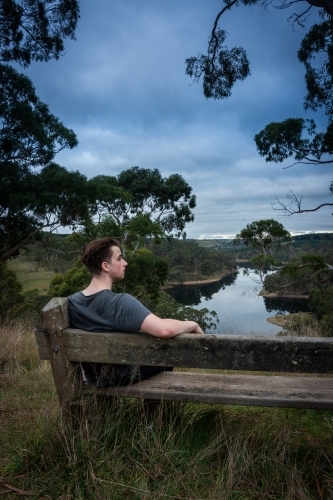Man Sitting on Bench above a lake on a stormy afternoon - Australian Stock Image