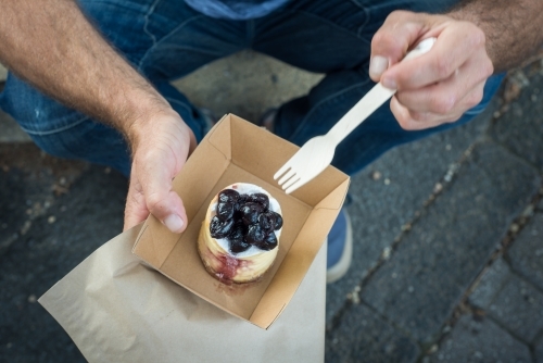 Man sitting on street curb eating bakery sweet - Australian Stock Image