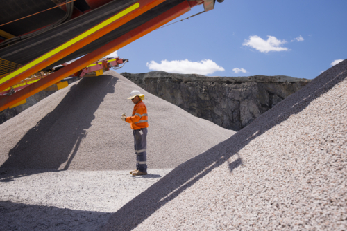 Man standing in between piles of aggregates near the crusher. - Australian Stock Image