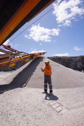 Man standing in between piles of aggregates near the crusher. - Australian Stock Image