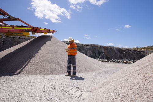 Man standing in between piles of aggregates near the crusher. - Australian Stock Image