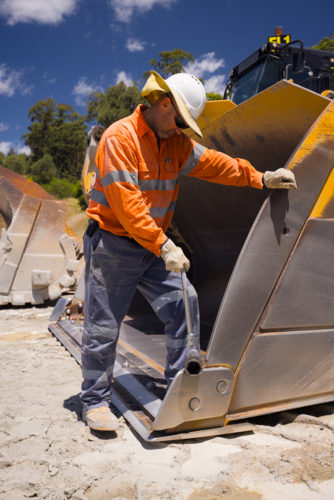 Man standing inside the bucket of a payloader. - Australian Stock Image