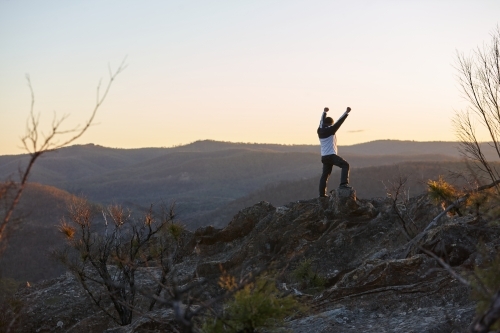 Man standing looking out over mountains on sunset - Australian Stock Image