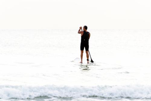 Man standing on board paddling and looking out to sea in very high light - Australian Stock Image