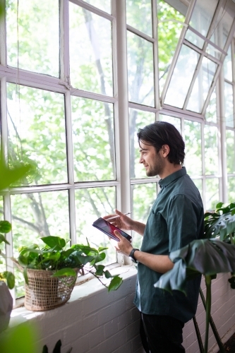 Man standing with device looking through windows - Australian Stock Image