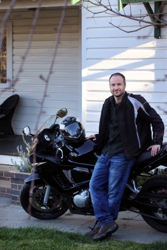 Man standing with motorbike outside of house - Australian Stock Image