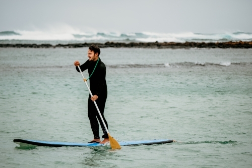 Man standup paddle boarding in the sea. - Australian Stock Image