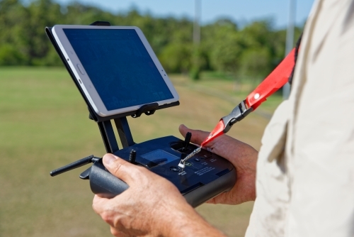 Man using his controller and tablet to fly and navigate his drone around the field - Australian Stock Image