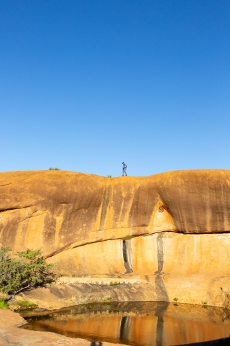 man walking across rock above a natural pool of water - Australian Stock Image