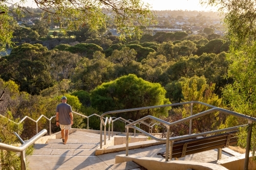 Man walking down stairs in parkland in early morning light - Australian Stock Image