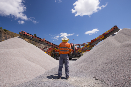 Man walking in between piles of aggregates near the crusher. - Australian Stock Image