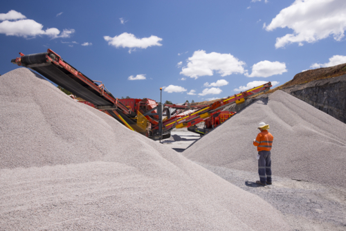 Man walking in between piles of aggregates near the crusher. - Australian Stock Image