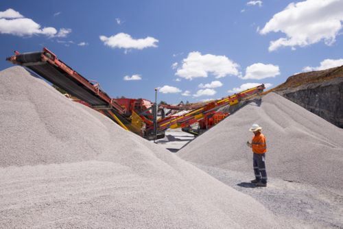 Man walking in between piles of aggregates near the crusher. - Australian Stock Image