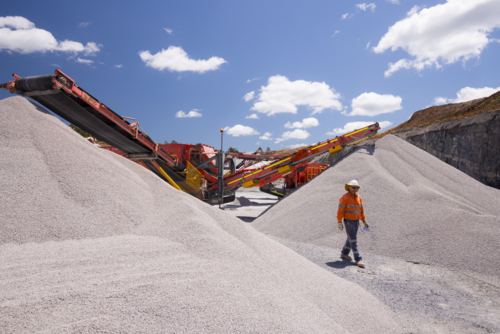 Man walking in between piles of aggregates near the crusher. - Australian Stock Image