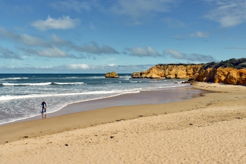 Man walking out to surf at a surf beach - Australian Stock Image