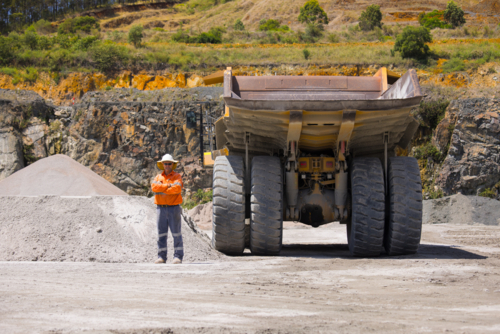 Man with arms crossed standing behind the hauler truck with massive wheels. - Australian Stock Image