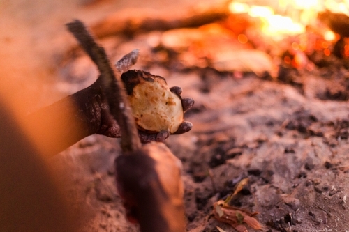 Man with food cooked on an open fire. - Australian Stock Image