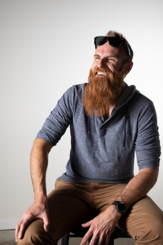 Man with long beard and sunglasses seated and smiling - Australian Stock Image