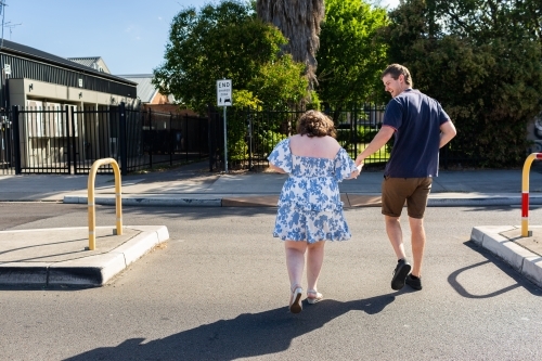 man working with person with a disability helping her cross the road safely holding hands - Australian Stock Image