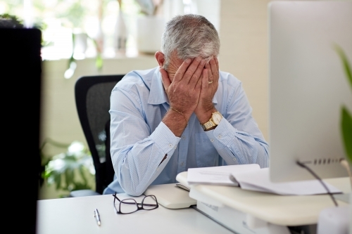 Mature business man sitting at a desk in a studio, thinking, worried - Australian Stock Image