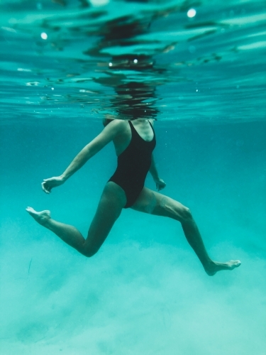 Mature woman's athletic body treading water from underwater perspective in ocean - Australian Stock Image