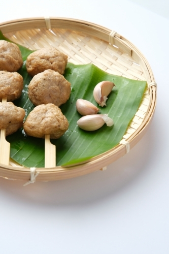 Meatballs on skewers served on a banana leaf inside the shallow woven basket. - Australian Stock Image