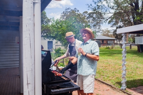 men laughing around barbeque in backyard at summertime family gathering - Australian Stock Image